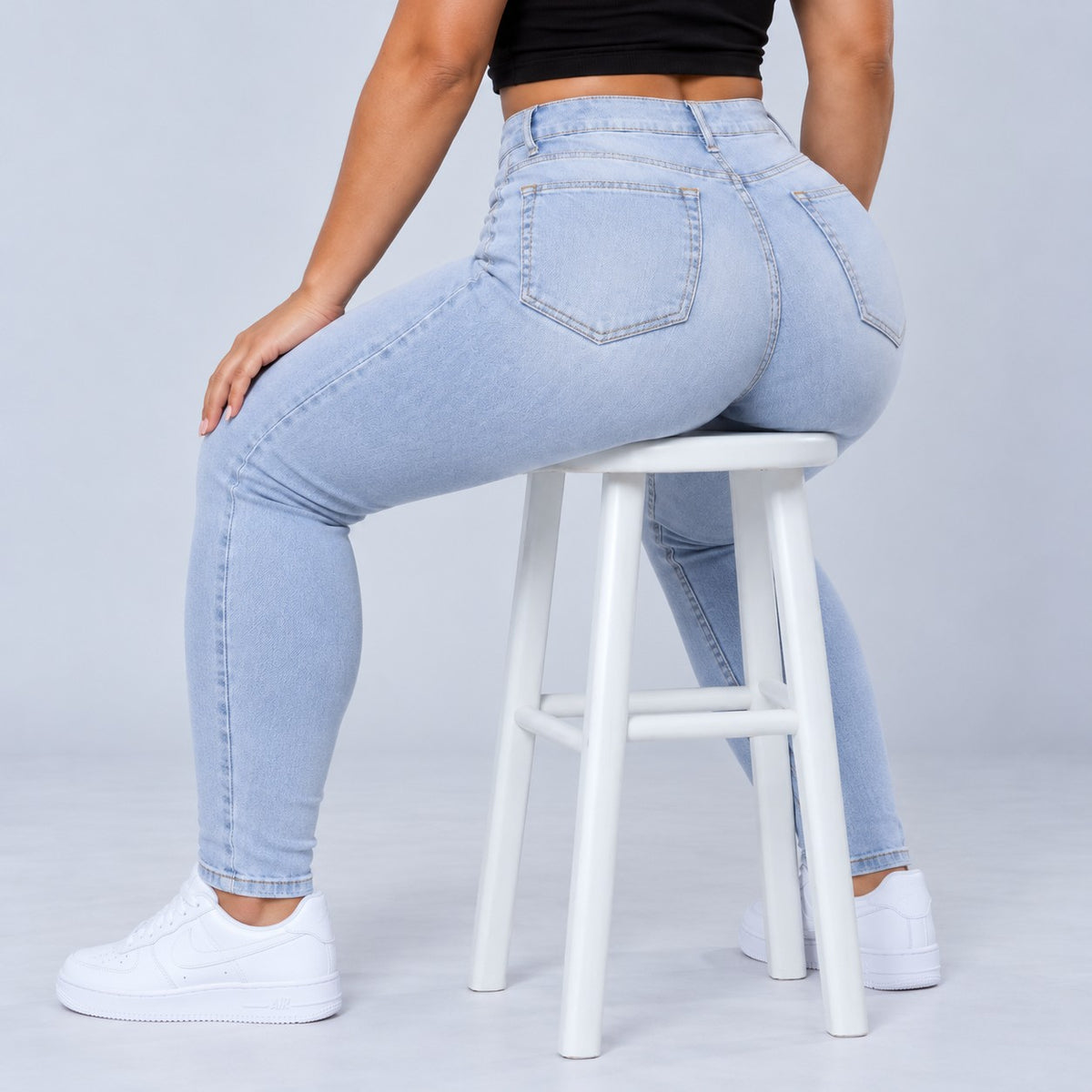 Sculpt Skinny BBL jean in light blue, seated on a stool