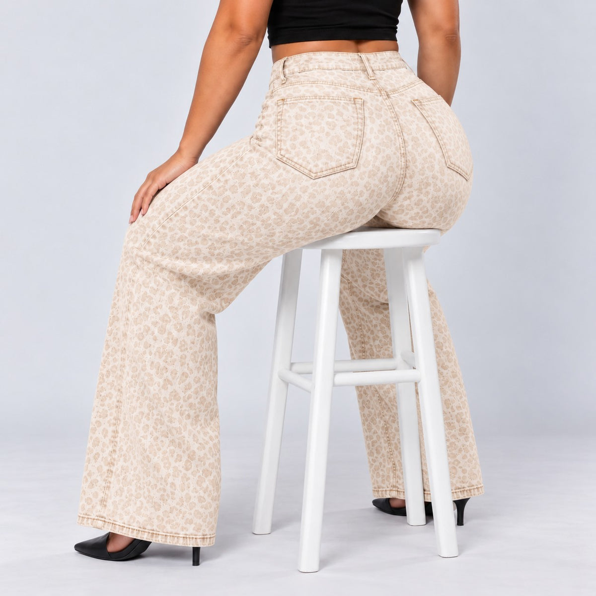 Sculpt Wide Leg BBL jean in white leopard, seated on a stool